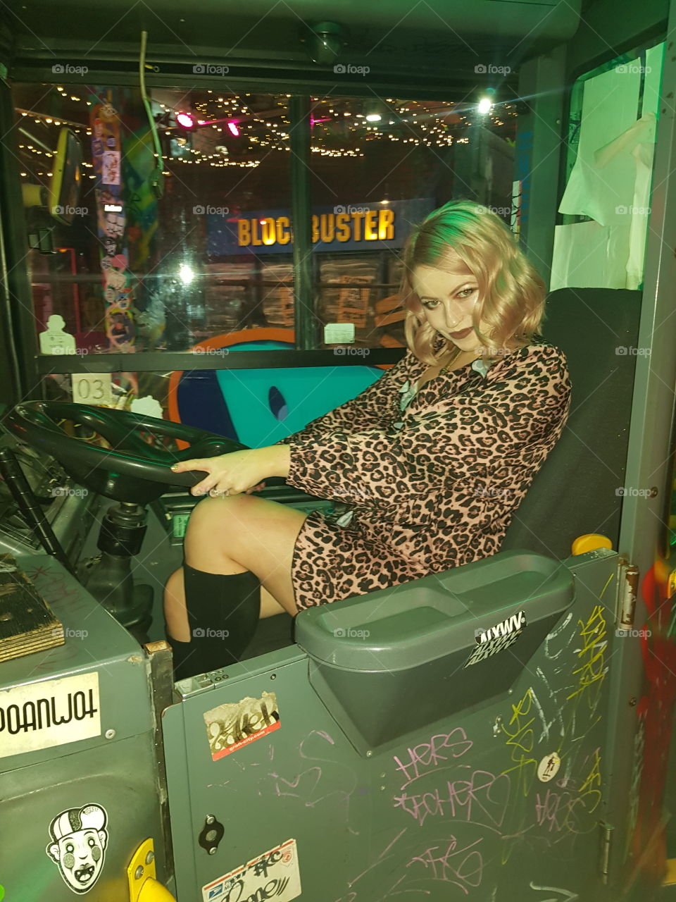 riding the bus at ghetto golf in Birmingham wearing leopard print dress and knee high boots. very drunk having fun posing for a photo around Christmas time. graffiti in the background oldschool blockbuster videos