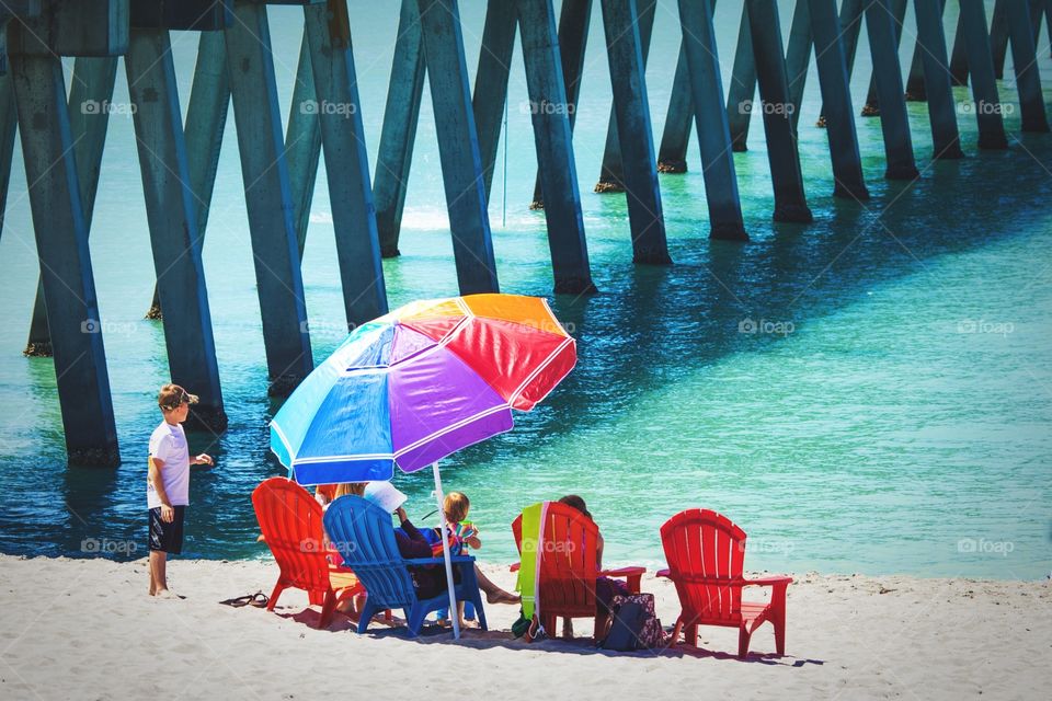 Colorful umbrella and chairs with family on Florida beach near a pier. Rainbow umbrella on a Florida beach with family on vacation