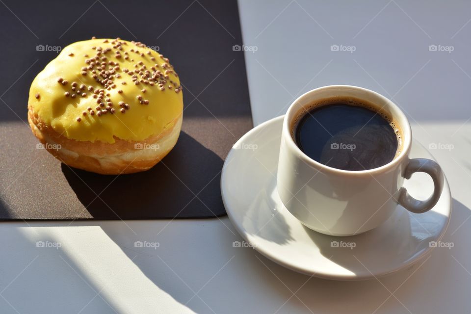 cup of coffee and bun sweet in sunlight and shadows on a white and brown background, morning routine