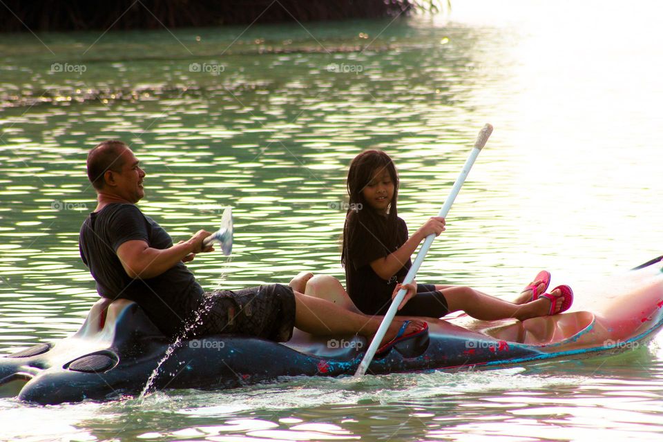 View of a man and a little girl sitting on a canoe pedaling the paddles they are holding during the day, canoe sports playing in the water : Jakarta, Indonesia 11 May 2023