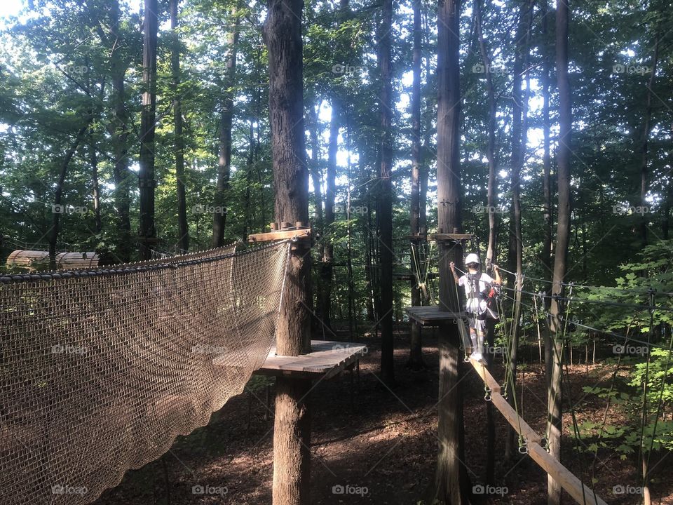 Boy balancing on beam in obstacle course located high up in the trees, great for mind and body 