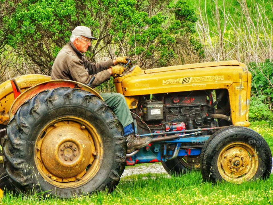 Old Farmer Riding A Yellow Tractor
