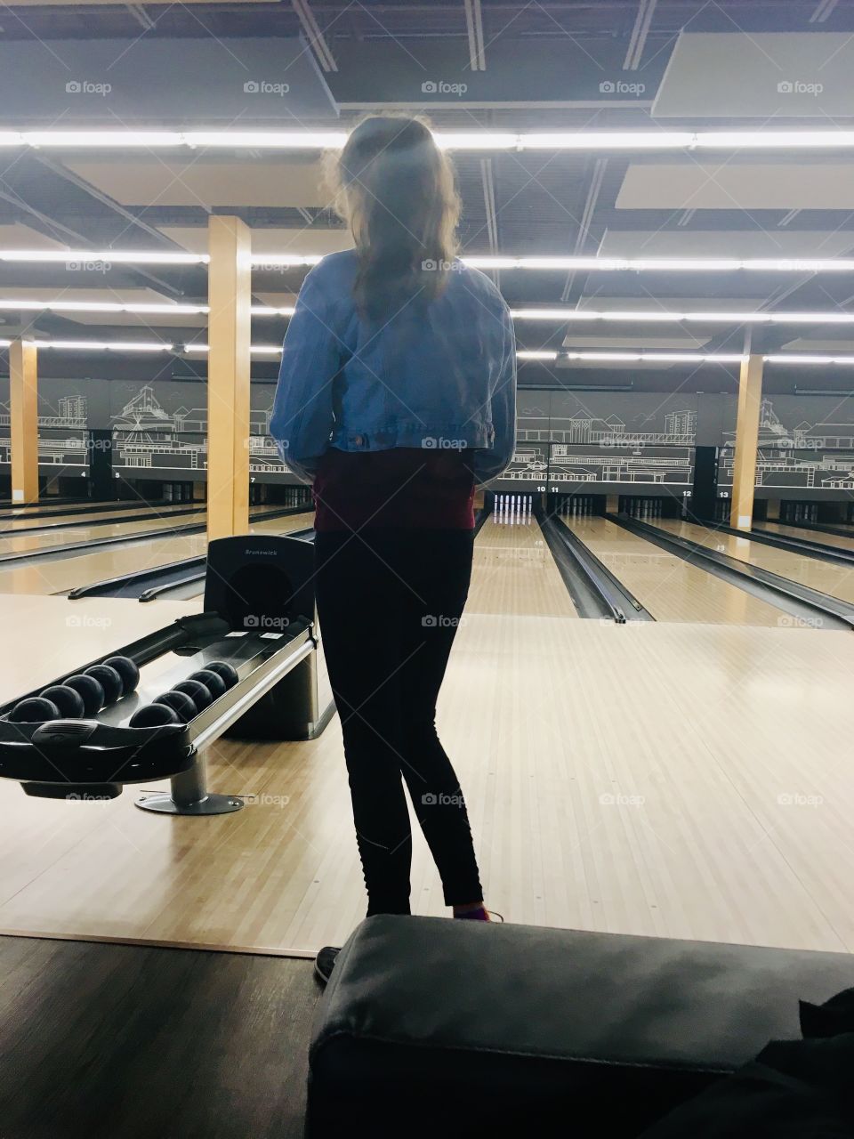 Teenage girl wearing jean jacket with long ponytail, bowling at a bowling alley. Fun winter night with friends. 