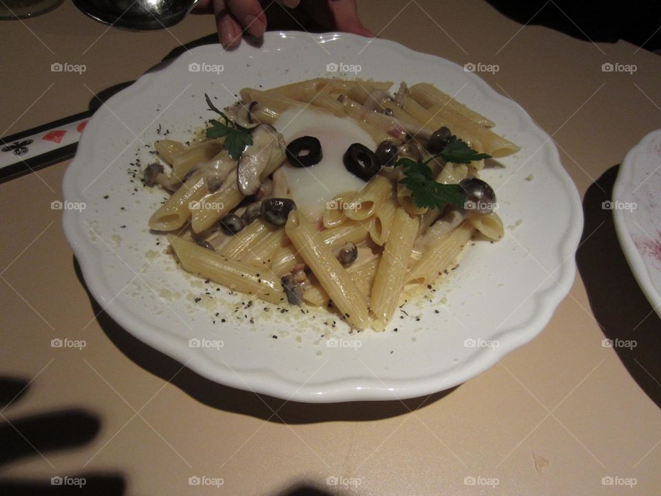 creamy white sauce italian penne pasta with black olives on a white plate. arranged to look like a face.