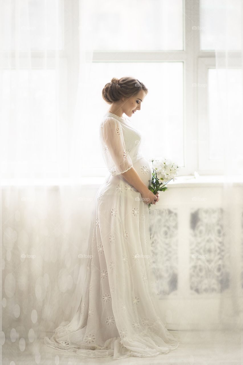 pregnant woman stands by the window and looks at a bouquet of flowers