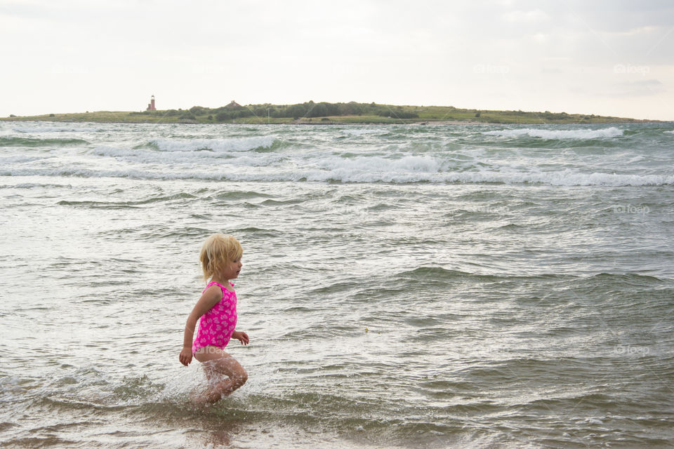 Girl playing at the beach of Tylösand outside Halmstad in Sweden. It's about to get stormy weather but the girl is having fun swimming and playing in the water.