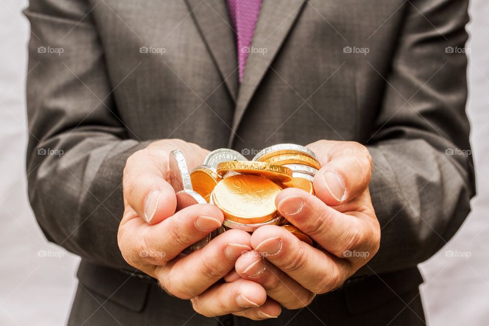 A close up of a man's cupped hands holding lots of gold and silver chocolate coins.