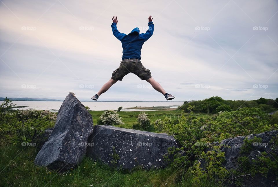 Man jumping in the air on the rock with view on Corrib lake in Galway, Ireland