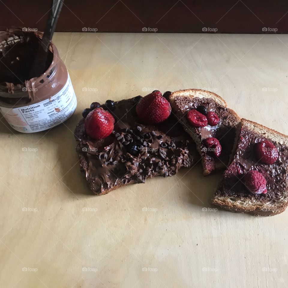 A delicious Nutella chocolate chip and strawberry and raspberry sandwich on wheat bread displayed on a cutting board in the kitchen next to the net tele-jar. USA, America