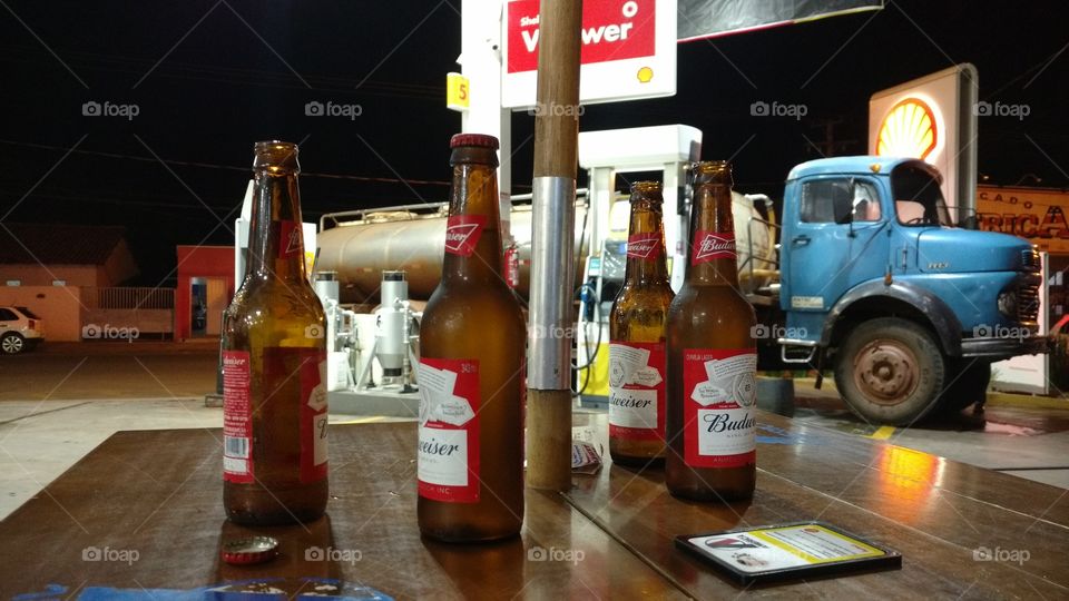 Garrafas de cerveja na mesa, caminhão em posto de combustível.