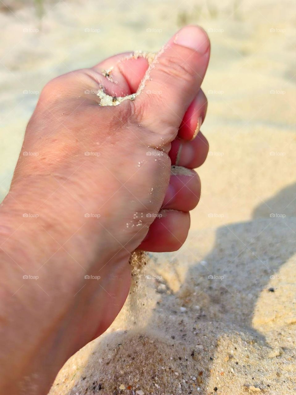 Small moments of happiness.  Yellow sand pours out of the fist of a woman's hand.  Sea shore.  Sun.  A tan
