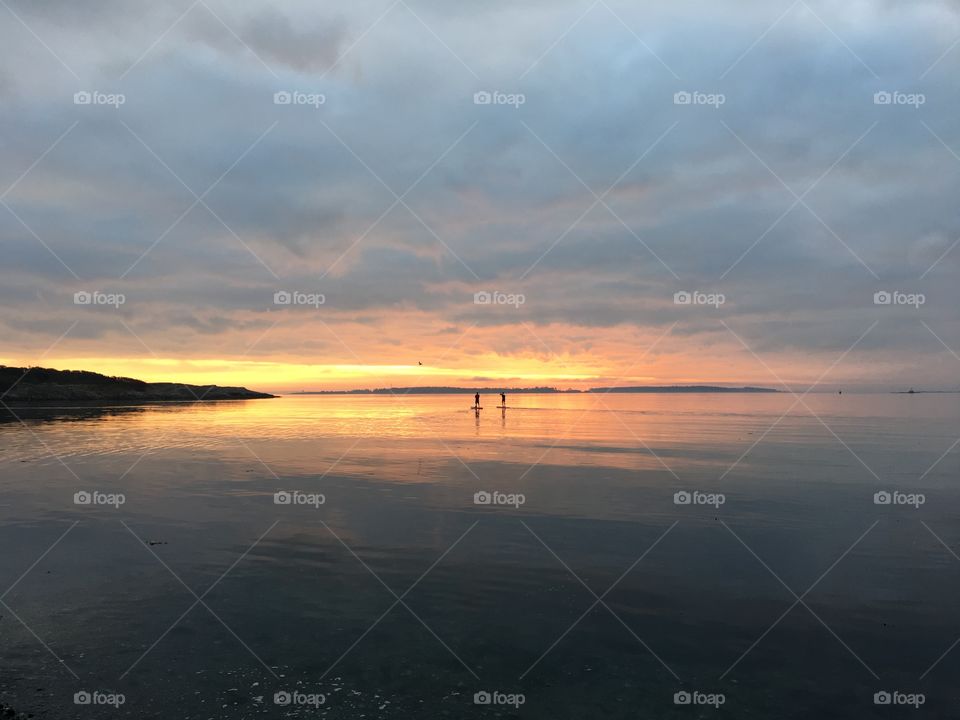 Paddle boarding on sunrise , glassy ocean and cloudy, yet calm sky  spreading morning serenity 