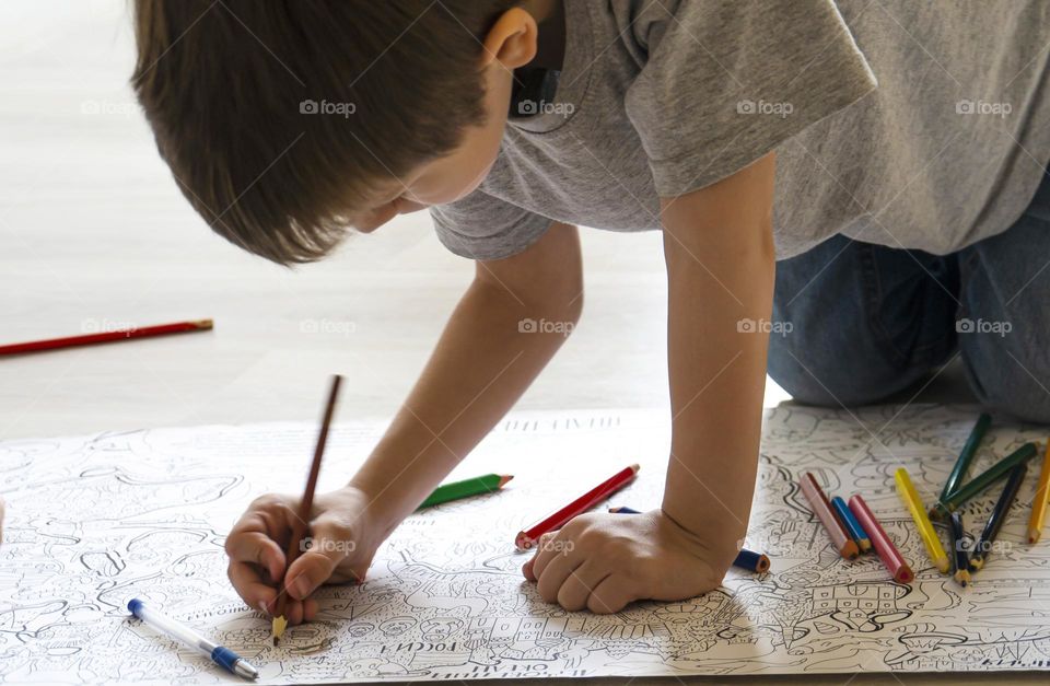 boy paints a large coloring book on the floor