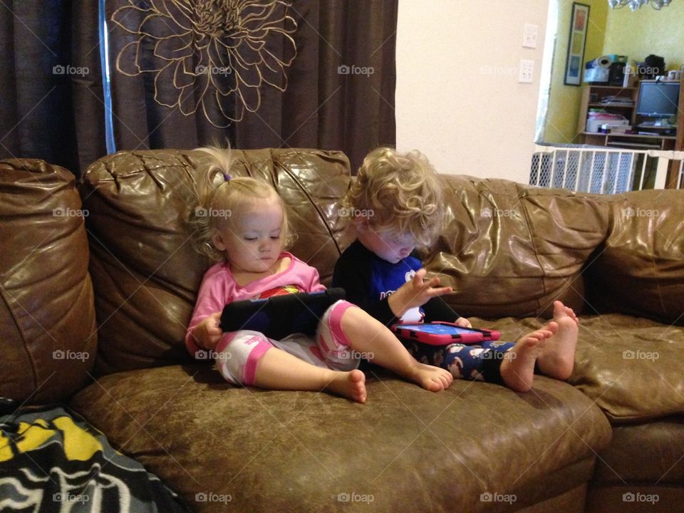 Boy girl twins using iPads on the couch