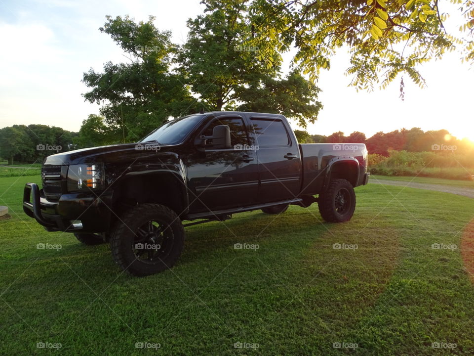 Black, Chevy 2500 at sunset on green grass with trees and sky behind it.