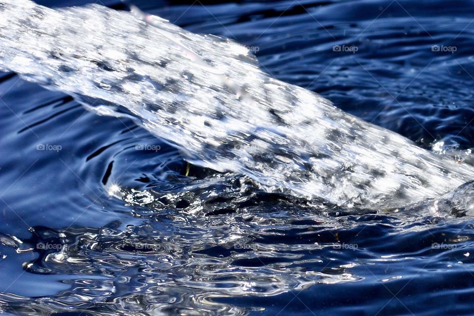 Isolated view of a strong stream of water, creating ripples reflecting a deep blue sky