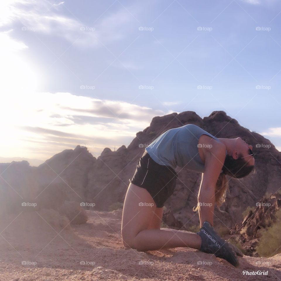 Girl doing the yoga camel pose in front of a mountain during a hike