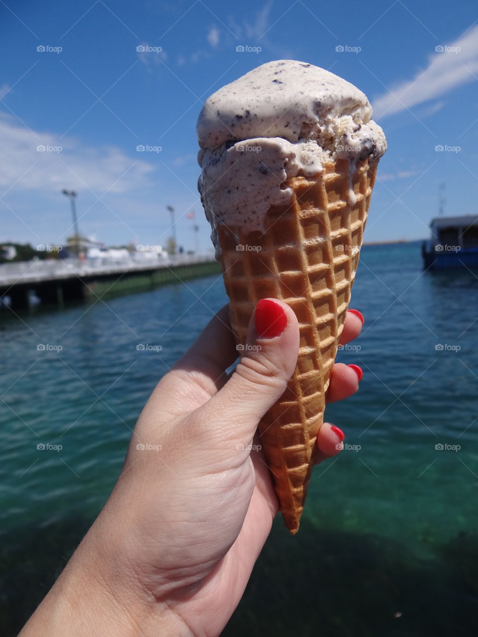 Hand holding ice cream. Feminine hand with manicure holding ice cream cone. Water in the background