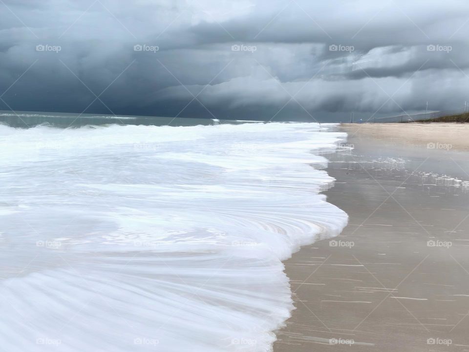 Atlantic Ocean Beach With Time In Motion Long Exposure Of The Waves On The Seashore During A Thunderstorm With Dark Grey Clouds.