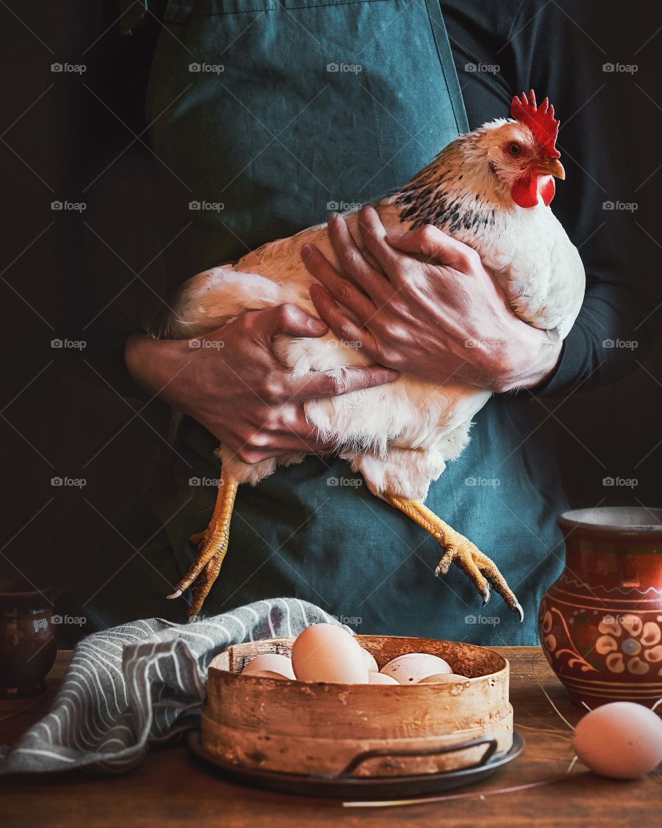 Man holding a hen against basket with eggs