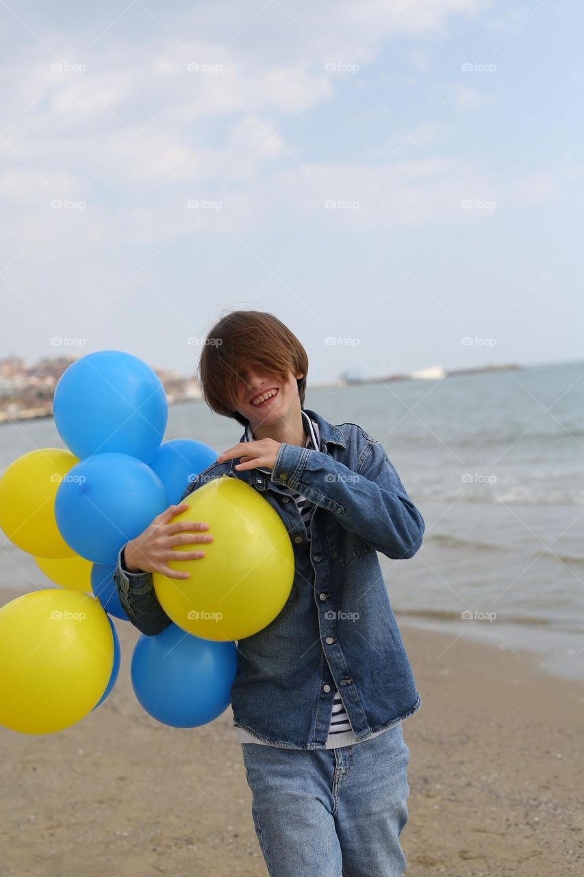 teenager with balloons in the hands of yellow and blue, runs along the seashore