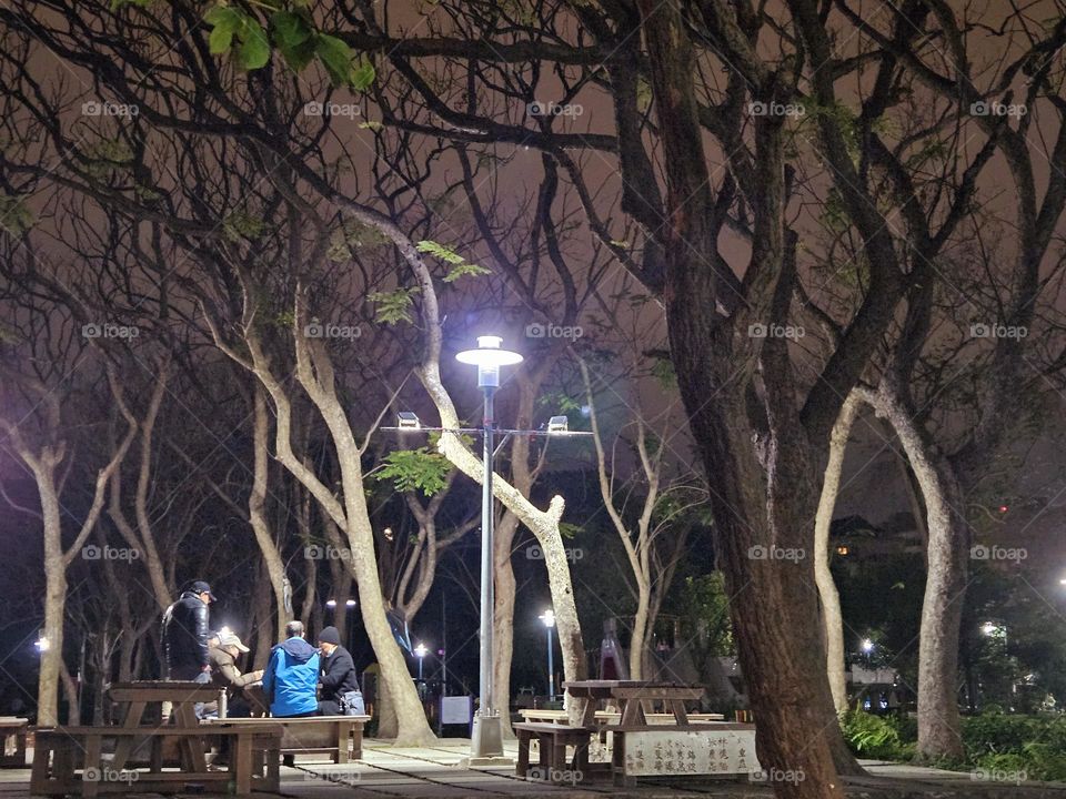 Old man playing chess in the park under the lights
