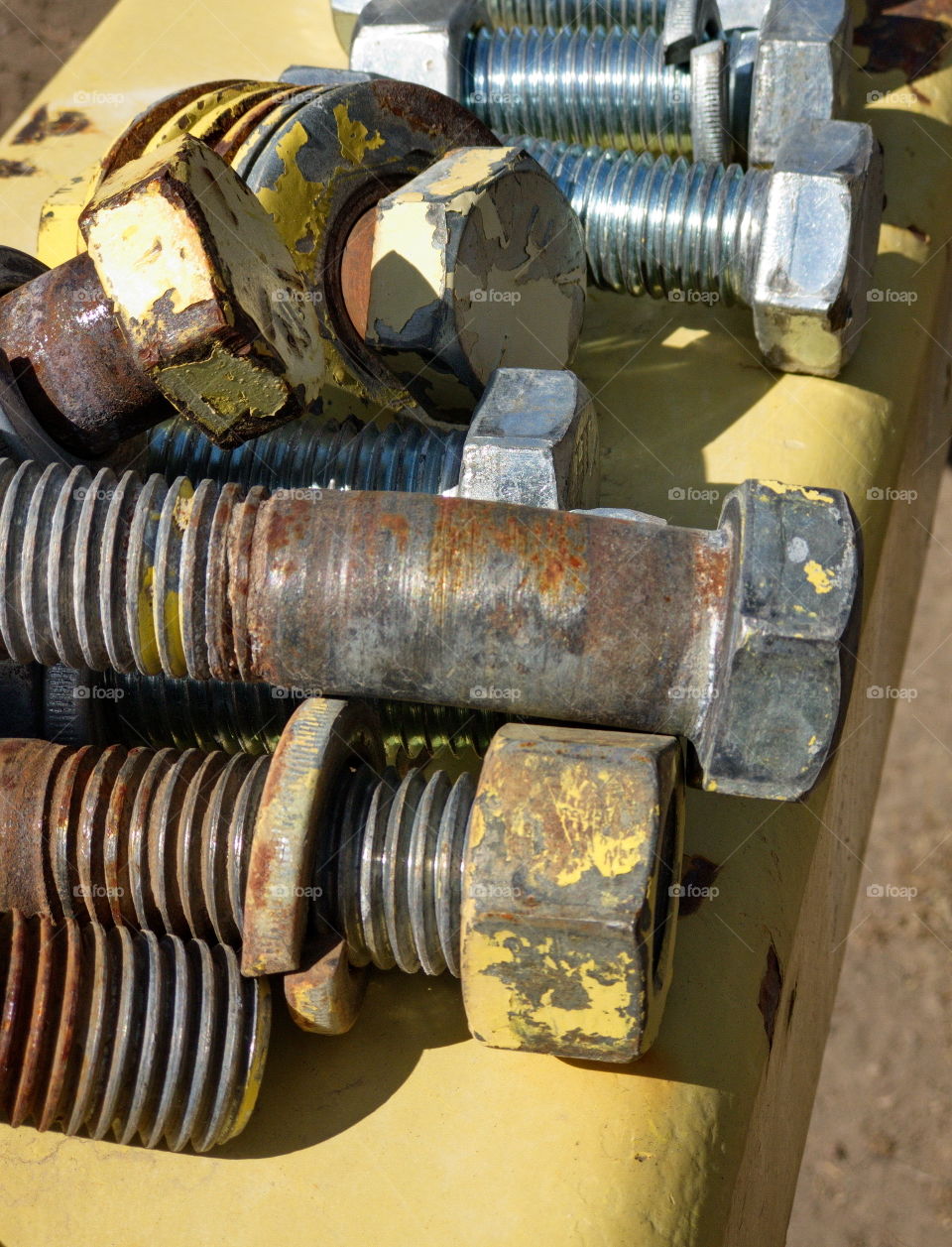 Closeup of the details and texture of yellow worn industrial sized bolts that have paint flakes amongst their rusted threads. 