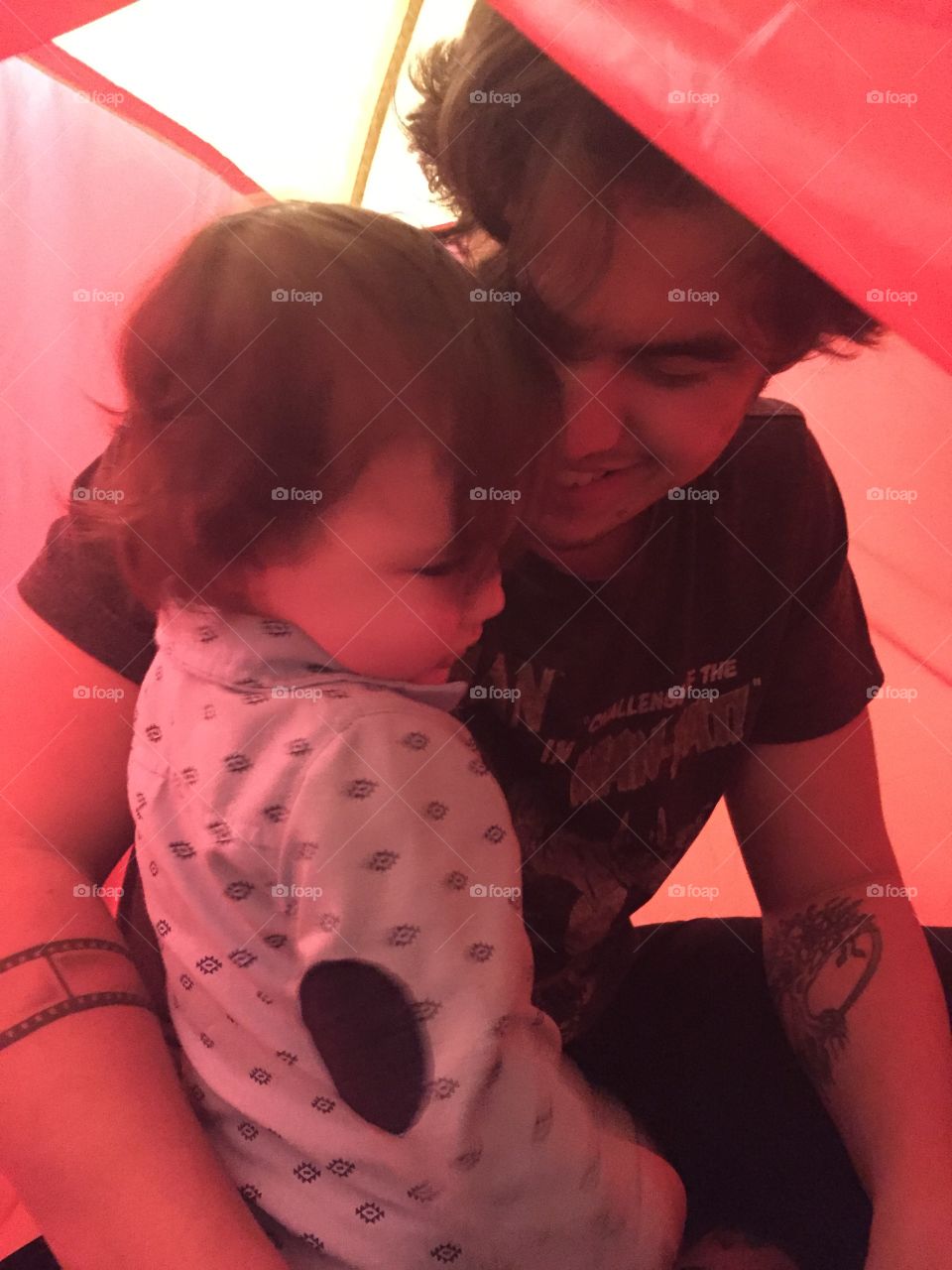 Father and son playing inside a small  orange pop up tent in the house and having a close moment. 