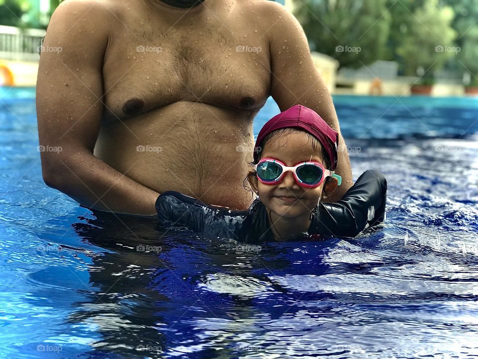 A girl swimming under her father’s care.