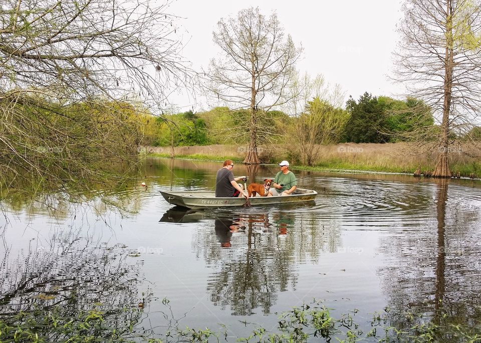 Two men and a dog fishing from a boat in the middle of a pond celebrating early spring