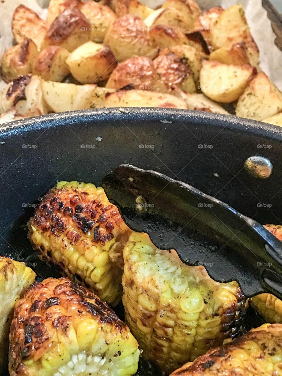 Roast corn on the cob and roast potatoes home cooking closeup