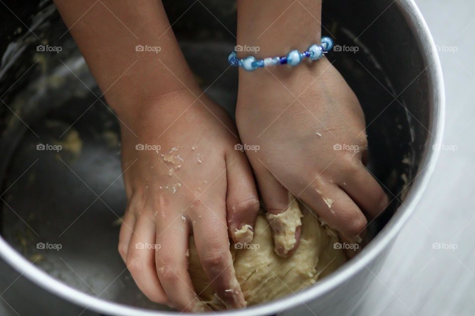 Child's hands with a blue bracelet are mixing a bread dough