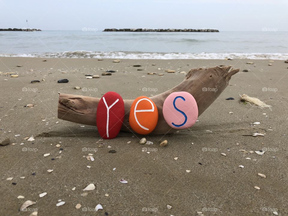 Yes word with colored stones on wood with sea and beach background