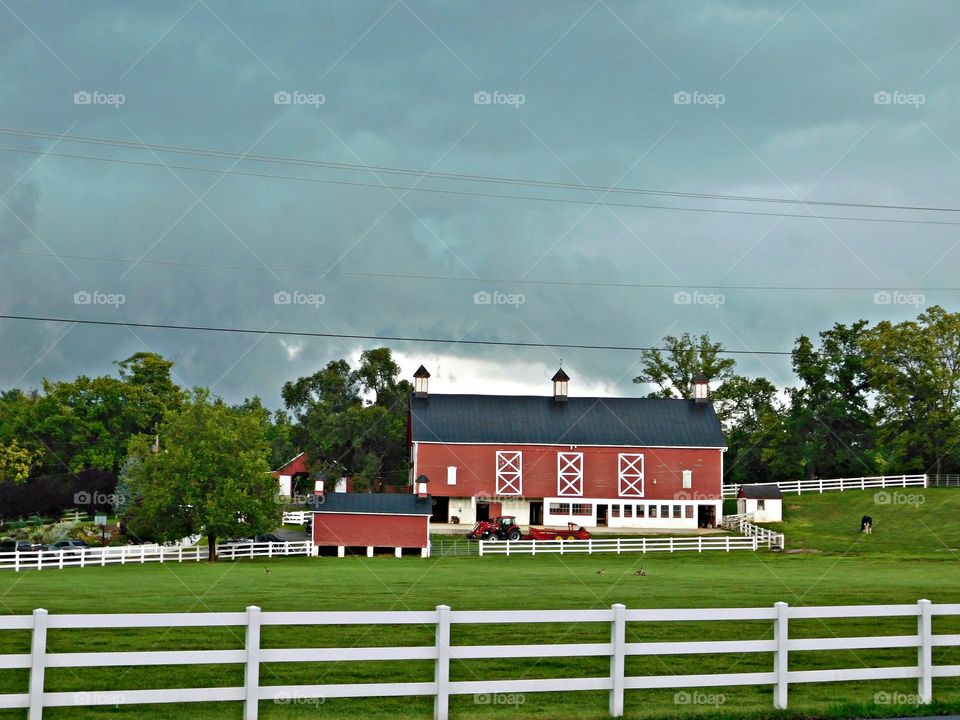 Vacation Series: Countryside - large red barn with a white fence around it. Dark clouds in the sky