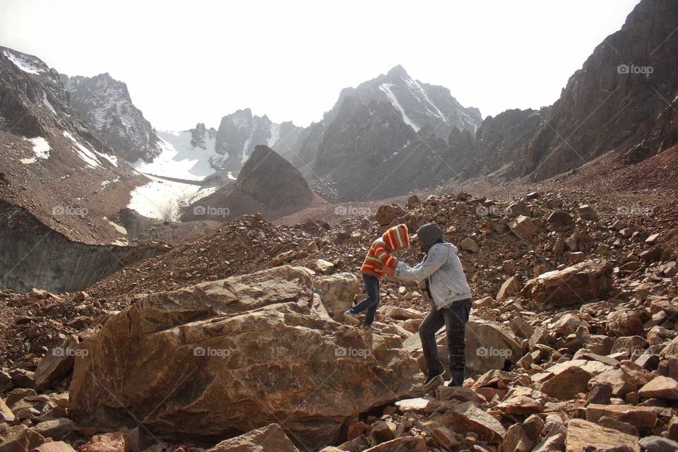 Dad helps daughter down a boulder on a glacier in the mountains
