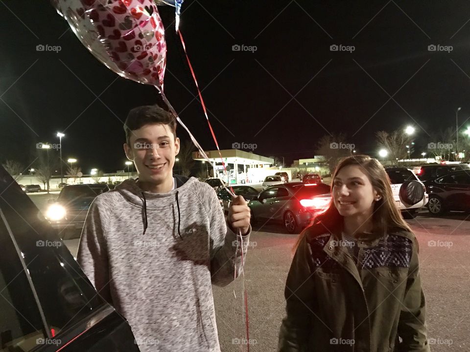 Happy couple standing by car with holding balloon at night