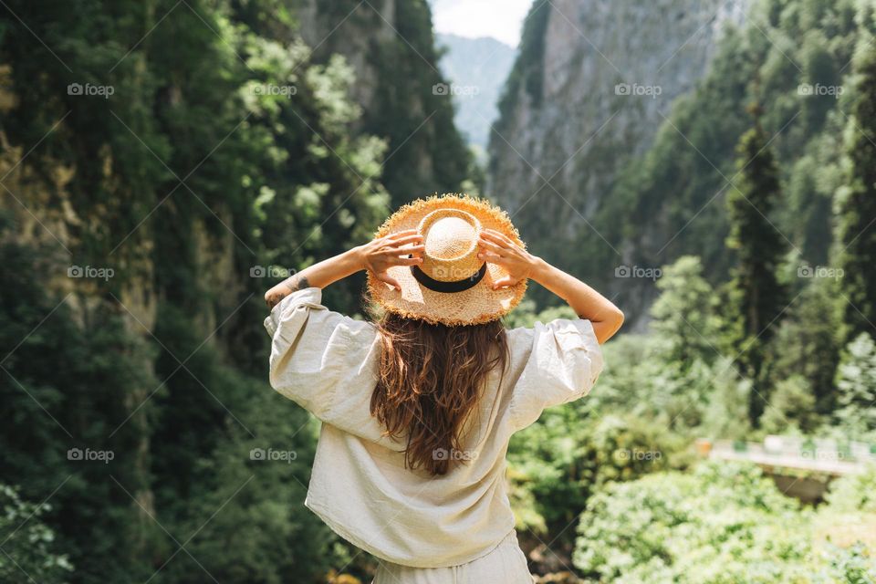 Young woman traveler with long blonde hair in straw hat looks at beautiful view of mountains, people from behind