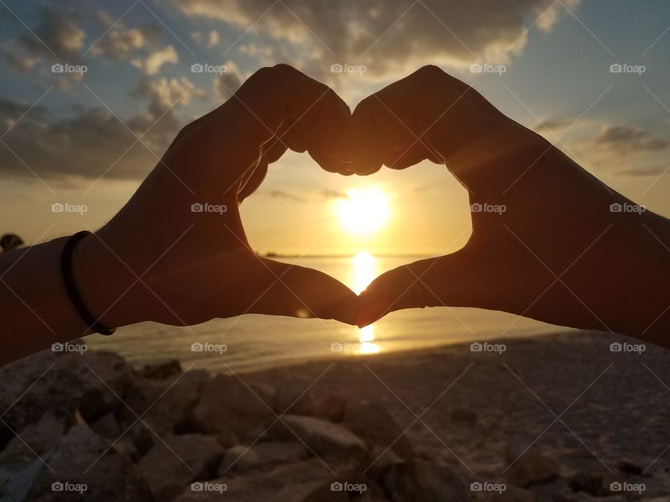 hands forming heart over the beach sunset