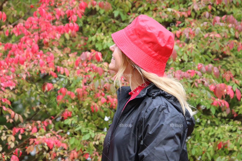 Smiling woman wearing with red hat in autumn looking at red leaves in background