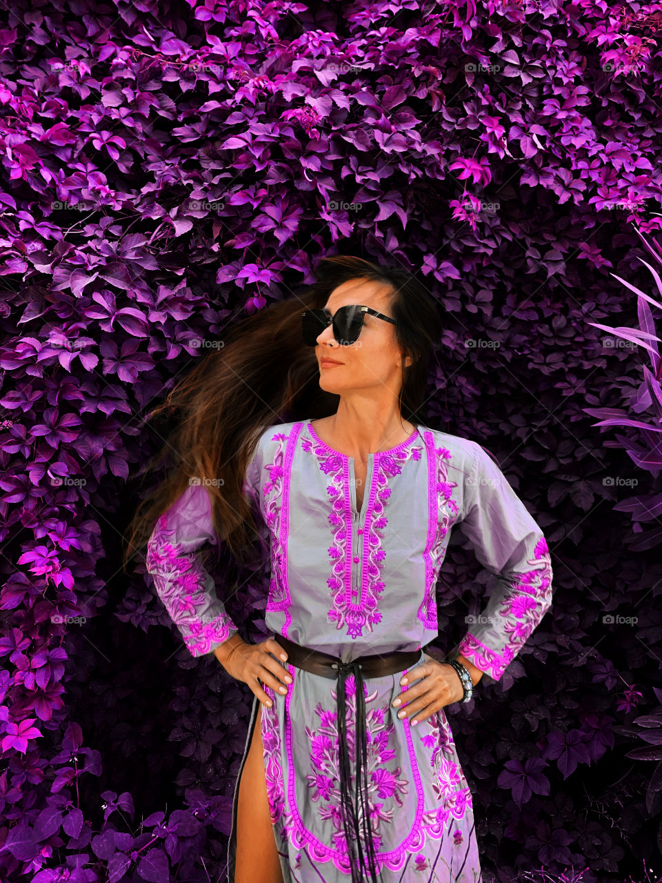 Young woman with long hair in purple dress standing in front of a purple plant 