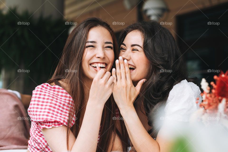 Happy smiling beautiful brunette young women friends in summer clothes having fun at the summer city street