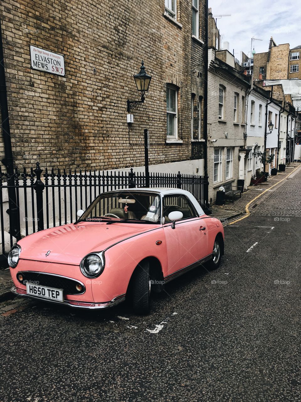 Pink Figaro car on a cobblestone street in London. Mews, old buildings and architecture. 