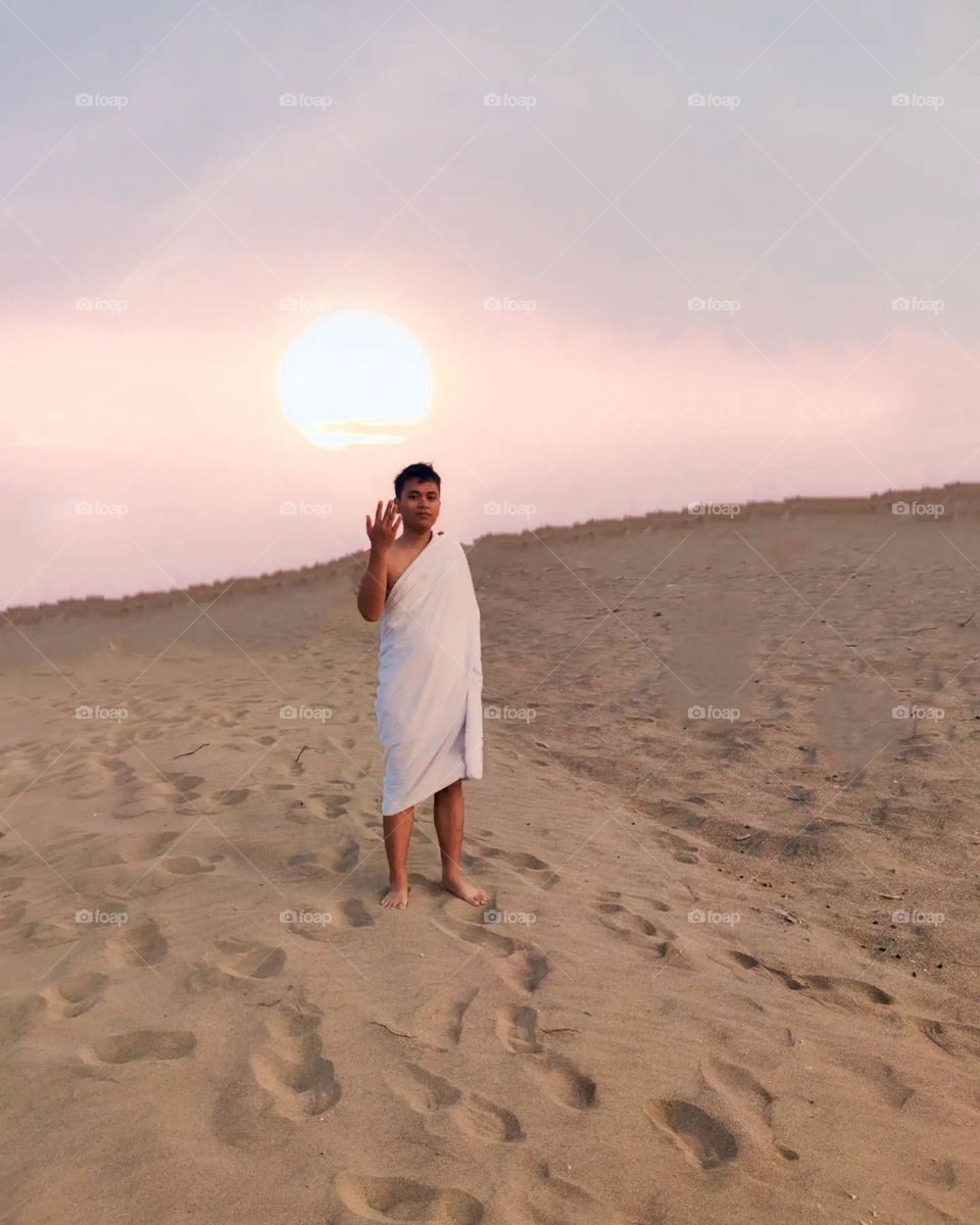 Long distance view of a man standing on a sand beach with the sunset in the background