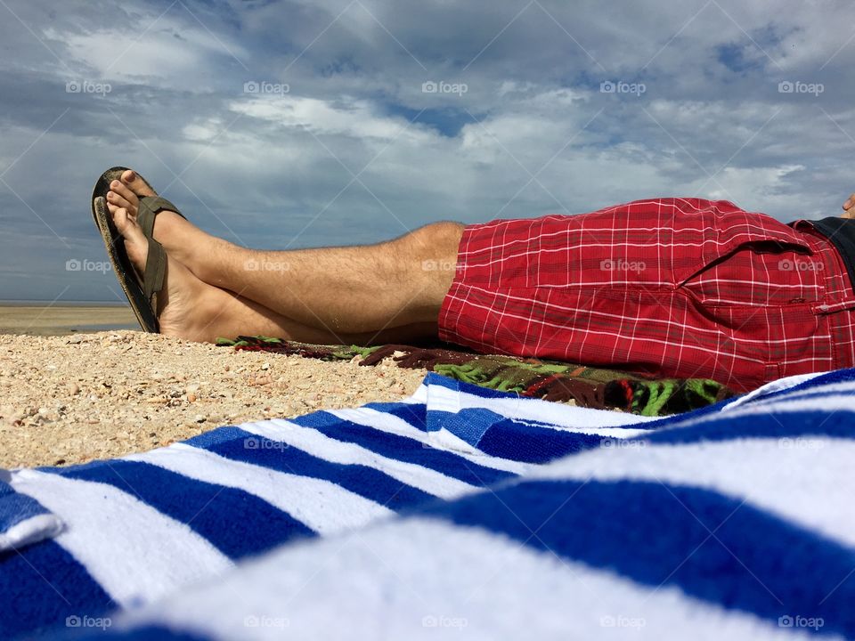 Man wearing red shorts on tropical beach, torso legs and feet only 