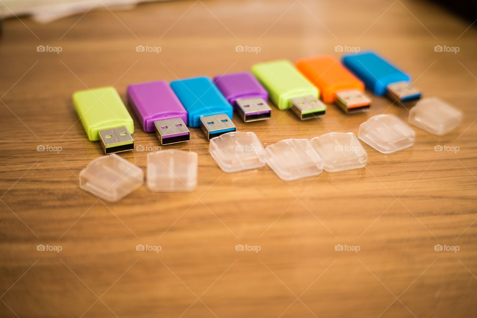 Multi-colored flash drives for working with documents, saving and transmitting, sharing files on a wooden texture table close-up.