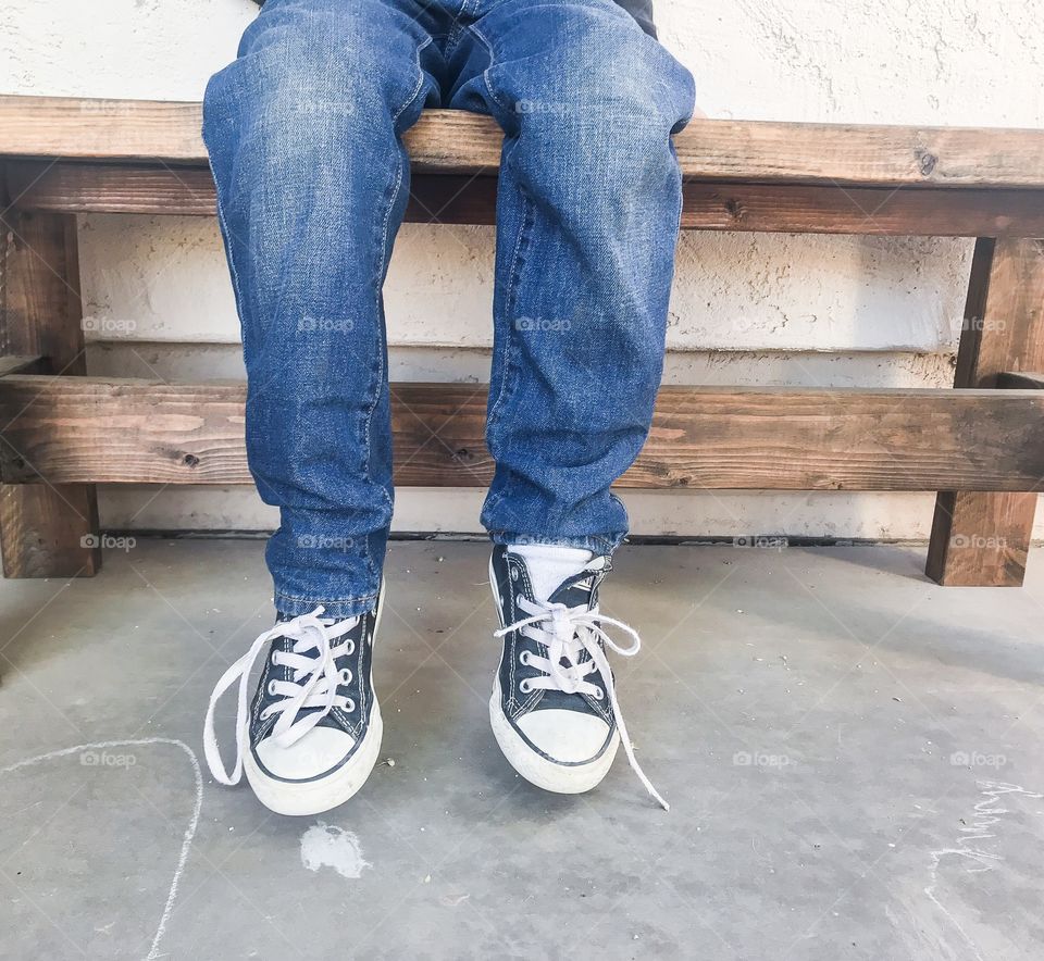 Boy legs sitting on a bench wearing blue jeans and converse shoes 