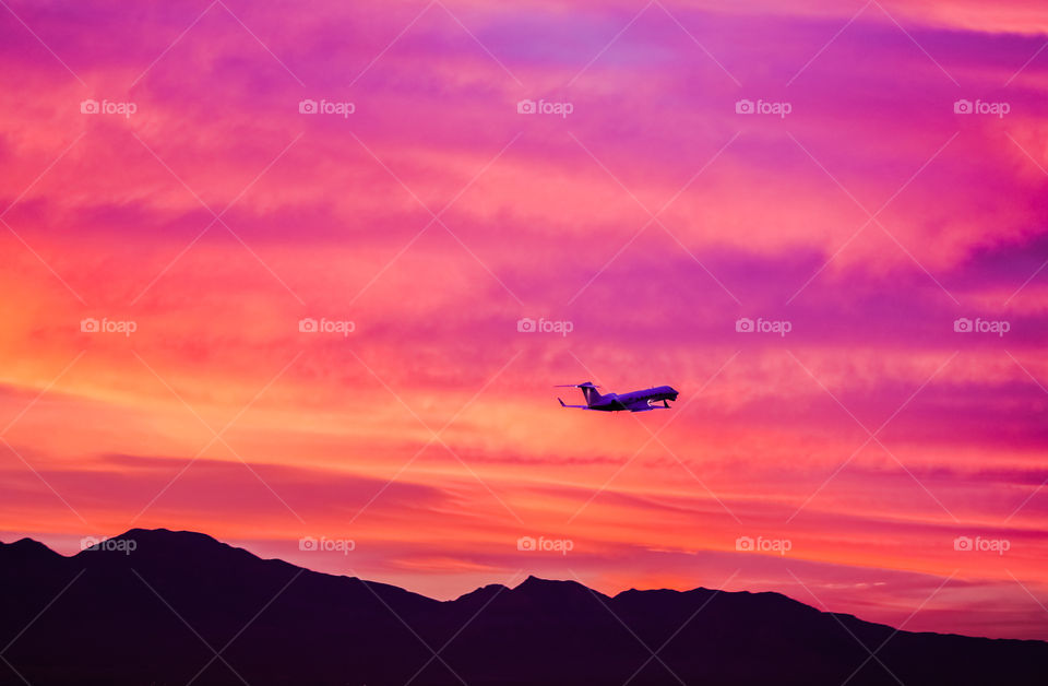 Plane flying over Southern Nevada mountain range into the sunset.
