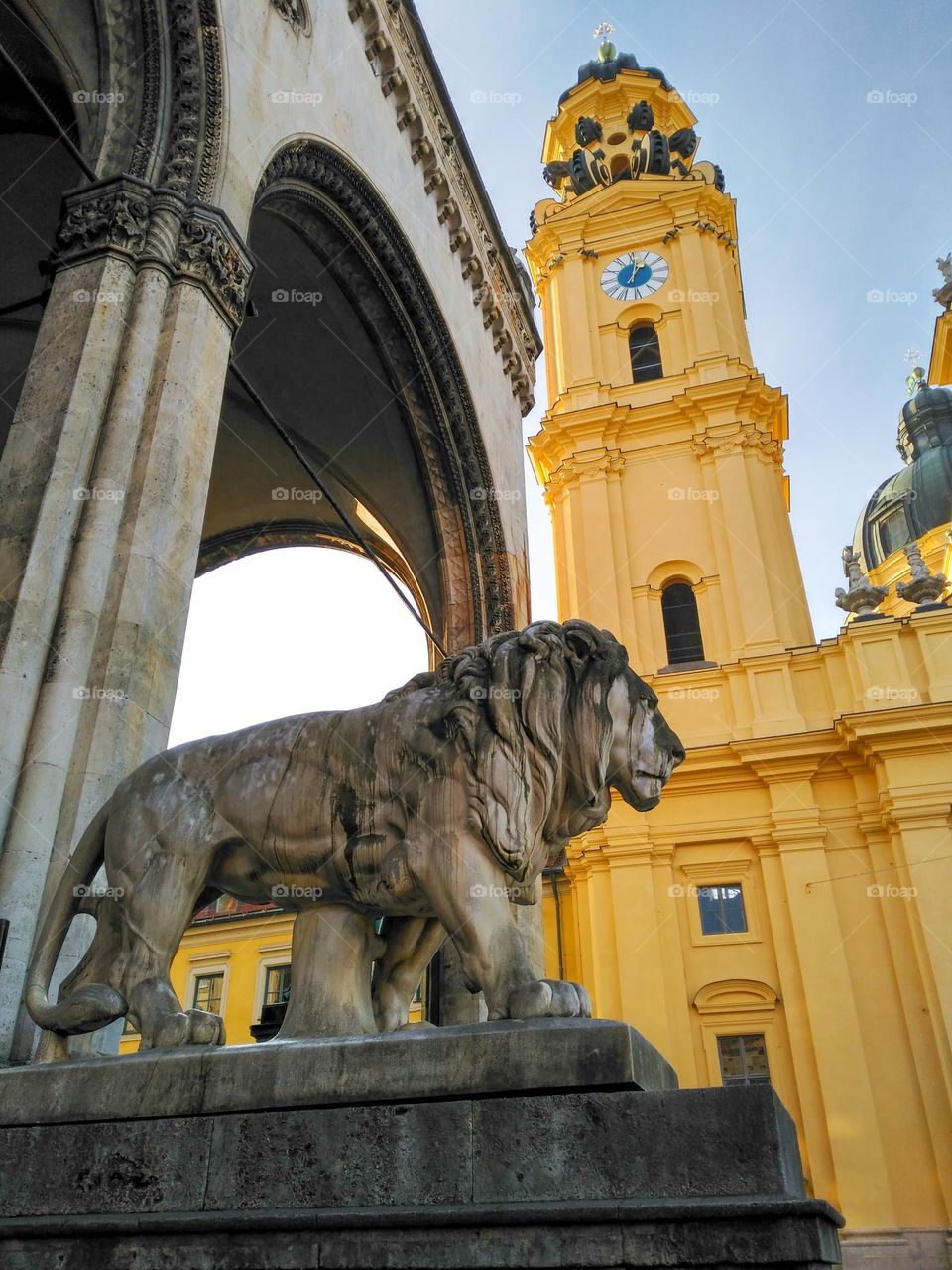 Sculpture of a lion set against a yellow buildingin and a clear sky Munich, Germany.