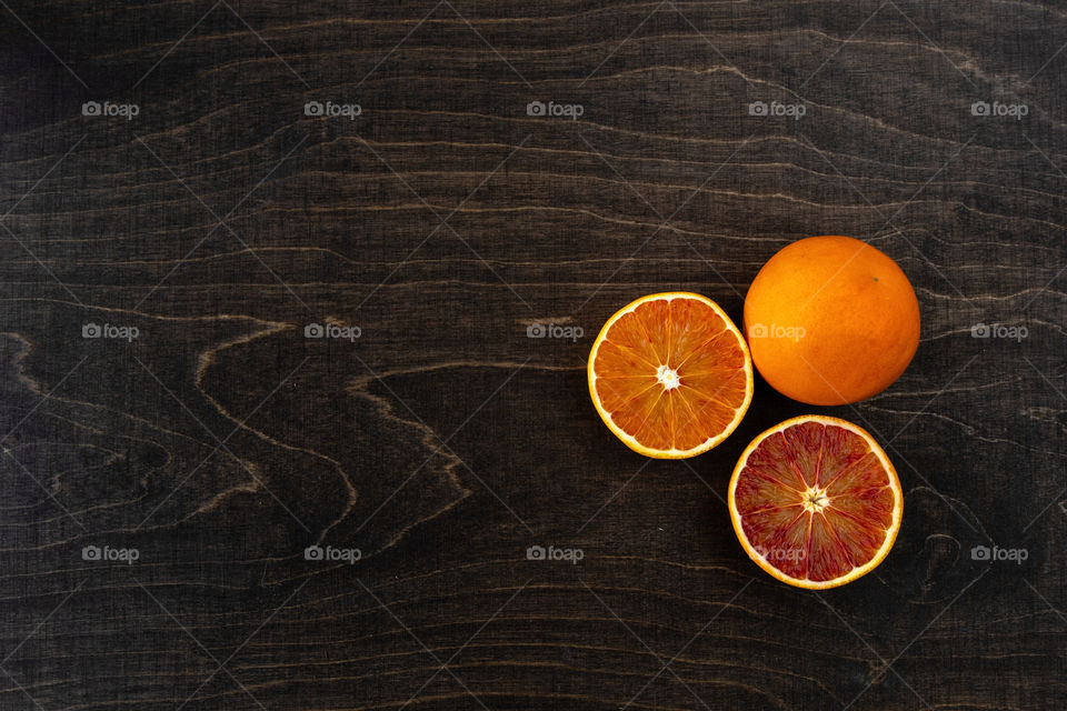 A closeup photo of vibrant organic blood oranges on a dark wooden  background with copy space.