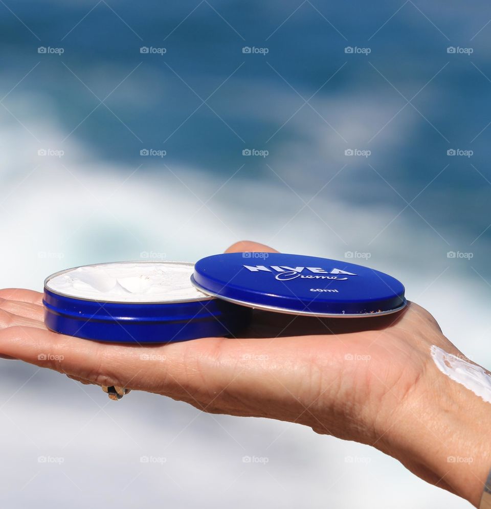 Nivea Creme moisturiser in the familiar little blue tin, in the flat palm of my hand, against the blurred backdrop of the Great Australian Bight, ocean. Skincare beauty product 